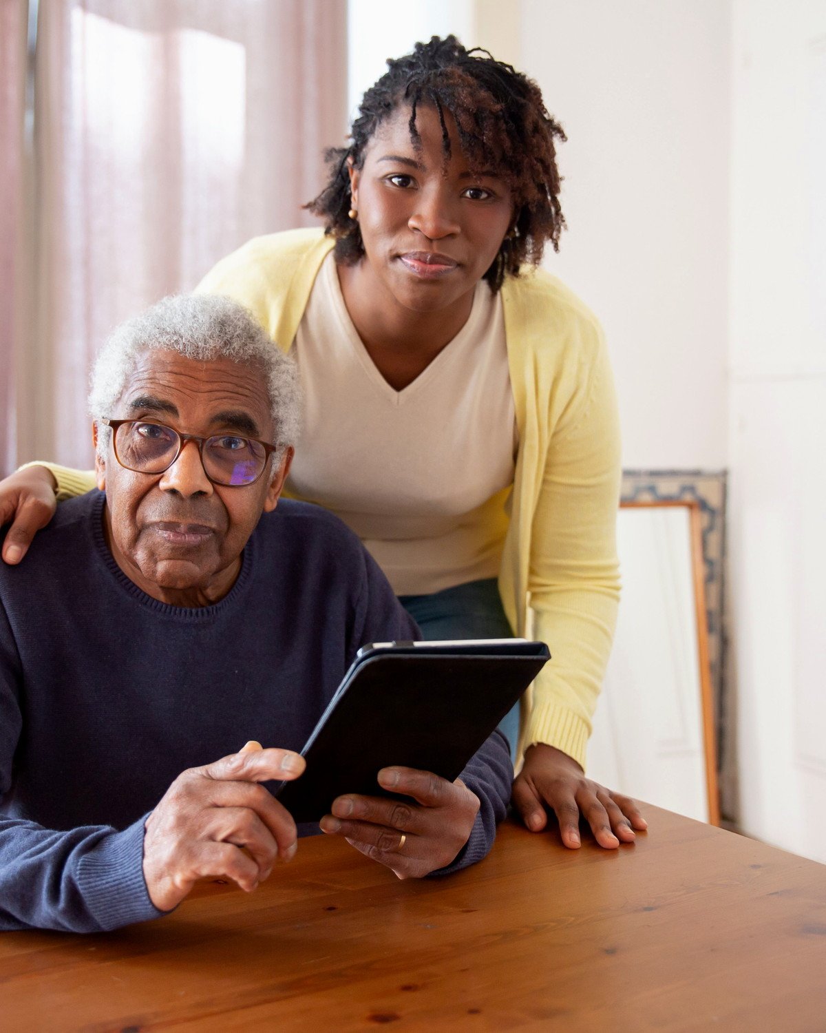 Pessoa idosa e cuidadora consultando informações em um tablet.